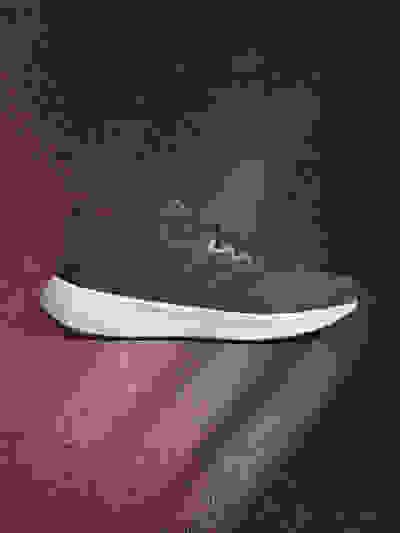 A gray athletic shoe with white soles is displayed against a dark, textured background with a reddish hue.