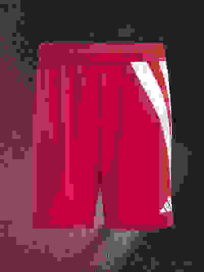 A pair of bright red athletic shorts with white stripes on a dark background.