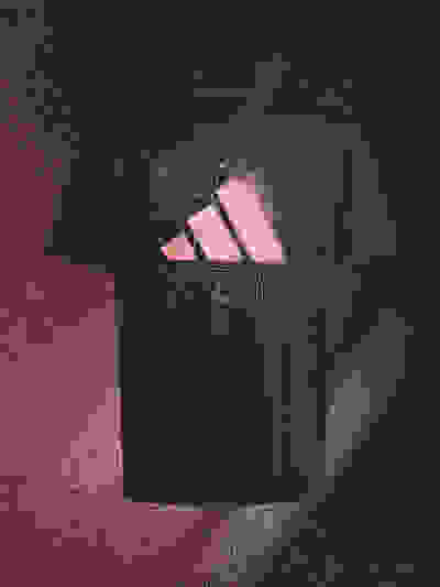 A black t-shirt with a pink fish-like creature design printed on it, set against a dark, textured background.