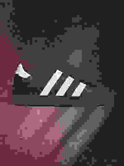 A black and white athletic shoe with three stripes on a dark red background, with a subtle lighting effect creating a dramatic atmosphere.