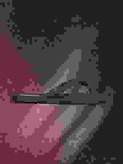 A black flip-flop sandal is shown against a dark, textured background with a reddish hue.