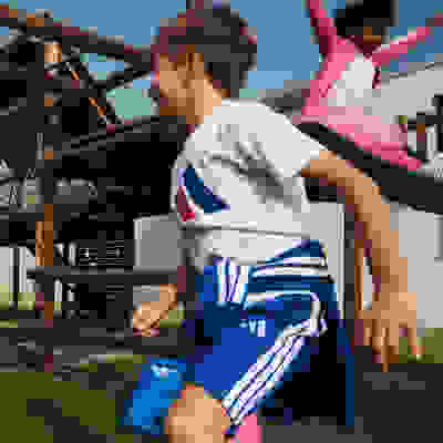 Two children, a boy and a girl, are playing on a wooden structure in an outdoor setting with a blue sky in the background.