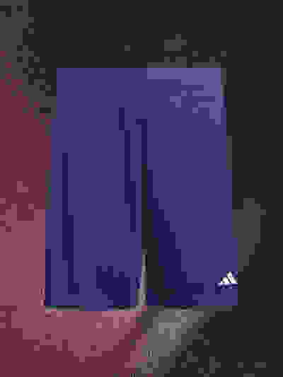 A pair of navy blue athletic shorts with the Adidas logo prominently displayed on a textured red background.