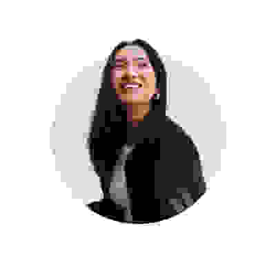 A smiling woman with long dark hair wearing a black jacket stands against a plain white background.