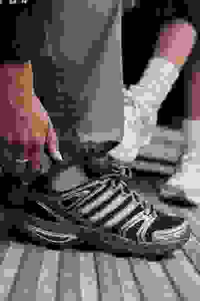 De afbeelding toont iemands onderlichaam, met een paar grijze sneakers en witte sokken die zichtbaar zijn op de voorgrond, tegen een donkere achtergrond.