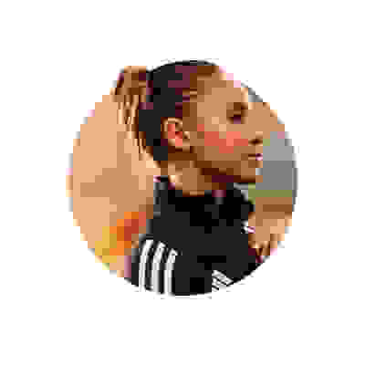 A young woman with a ponytail wearing a black athletic jacket stands against a warm, blurred background.