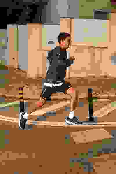 A person in athletic clothing is running on a crosswalk in an urban setting, with buildings and other structures visible in the background.