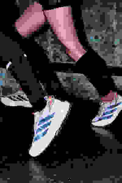 L'immagine mostra le gambe e i piedi di una persona che indossa pantaloni neri e sneaker bianche e blu, in piedi su una superficie di cemento.