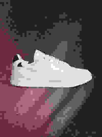 A white sneaker with black accents sits on a red and black textured background, casting a subtle shadow.