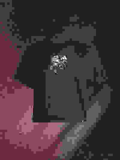 A black t-shirt with a graphic design on it, set against a dark, textured background with a reddish hue.