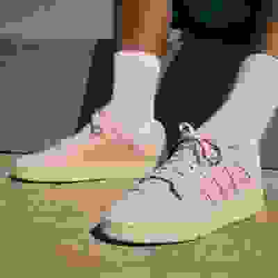 The image shows a pair of light-colored sneakers with white socks on a concrete surface.