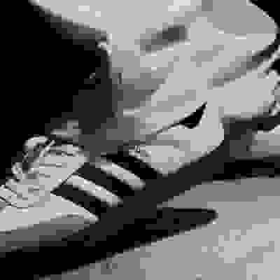 The image shows a pair of white and black Adidas Samba sneakers on a concrete surface.