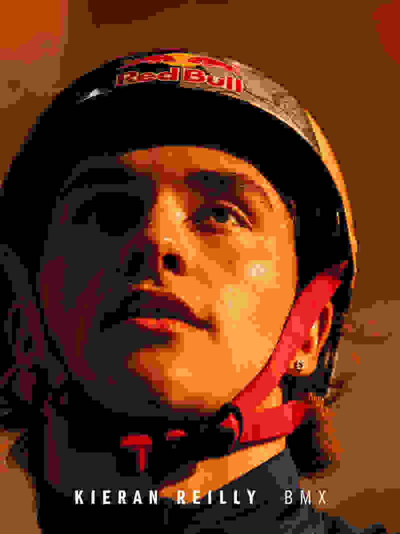 The image shows a close-up portrait of a person wearing a red and black helmet with the Red Bull logo, against an orange-tinted background, suggesting the individual is likely a BMX rider or athlete.