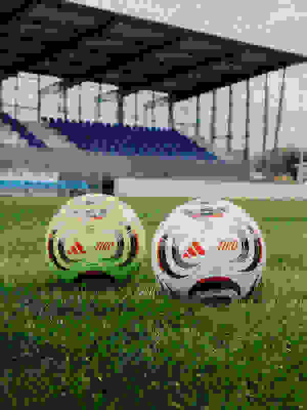 Two soccer balls with the Tiro brand logo are placed on the grass field of a sports stadium with empty blue seats visible in the background.