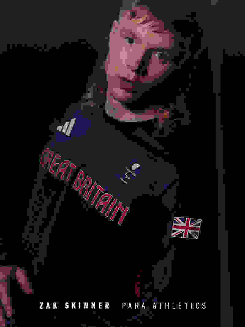 A young person wearing a navy blue "Great Britain" sports jersey stands against a dark background, their face partially obscured by the jersey's collar.