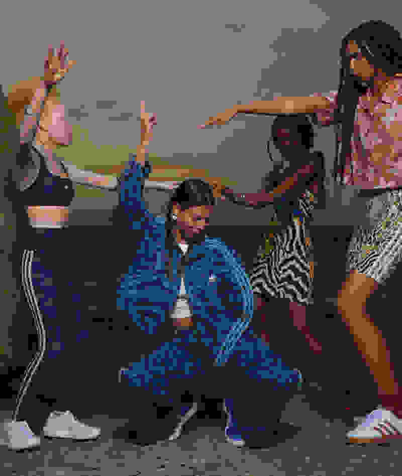 A group of young people, dressed in vibrant, patterned clothing, are engaged in a lively dance performance against a backdrop of a scenic outdoor setting.