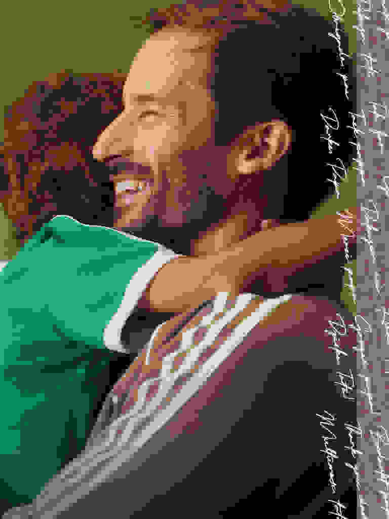 Un hombre con barba está abrazando a un niño pequeño, ambos con ropa verde y blanca, sobre un fondo liso.