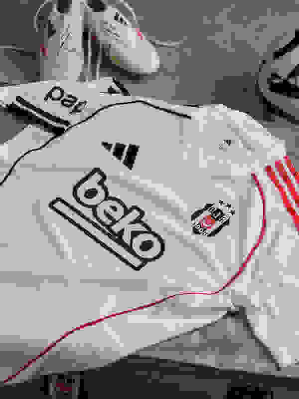 The image shows a white soccer jersey with the Beko logo, along with a pair of white and green soccer cleats and other soccer equipment.