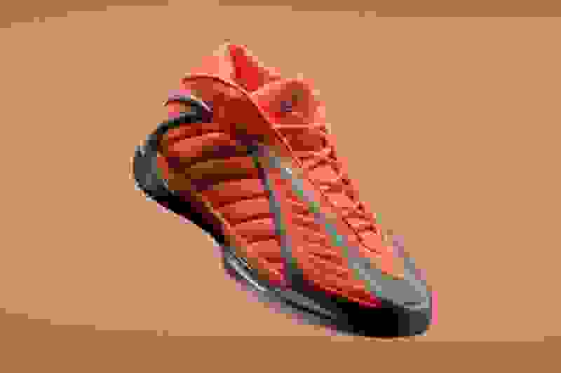 A vibrant, orange-colored athletic shoe with a sleek, futuristic design stands out against a plain, peach-colored background.