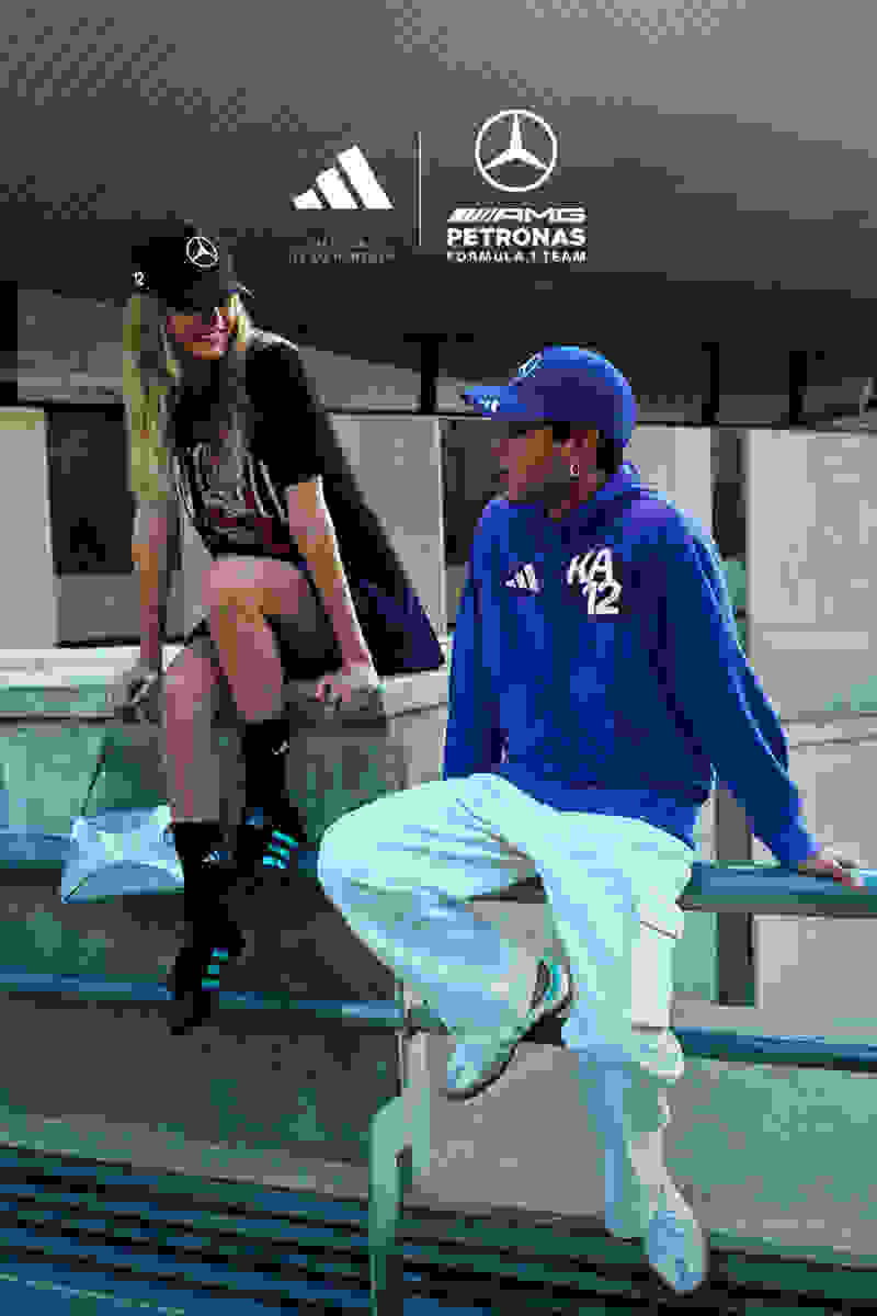 Two individuals, a woman and a man, are seated on a bench in an outdoor setting with sports-related branding visible in the background.