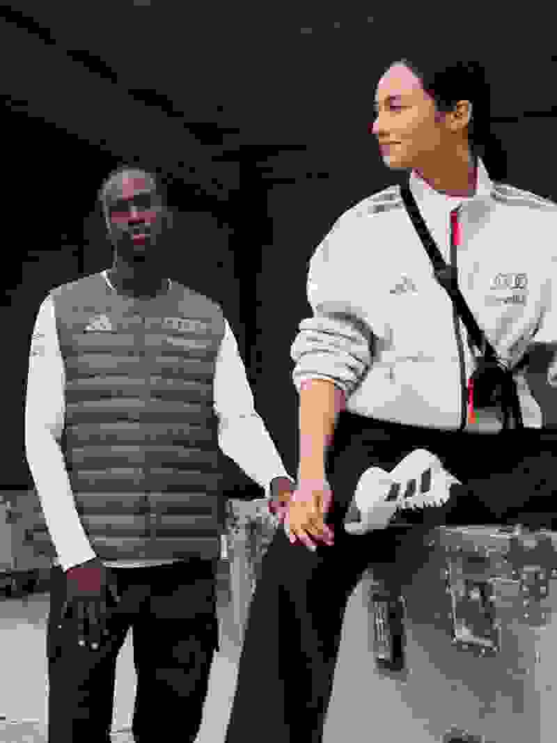 Two individuals, a man and a woman, are standing in what appears to be a backstage or storage area, with various equipment and cases visible in the background.