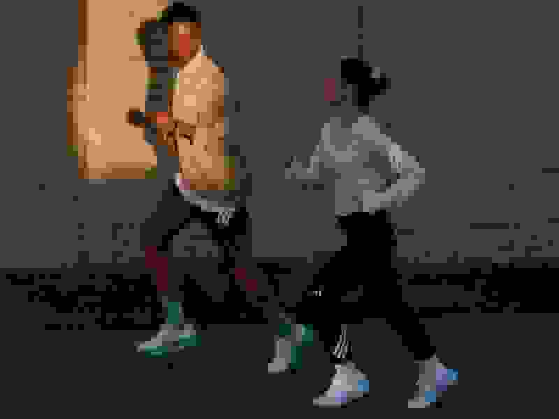 Two individuals, a man and a woman, are engaged in a lively interaction against the backdrop of a brick wall. The man is wearing a light-colored shirt and the woman is wearing a white blouse, and they both appear to be in motion, suggesting an energetic exchange.