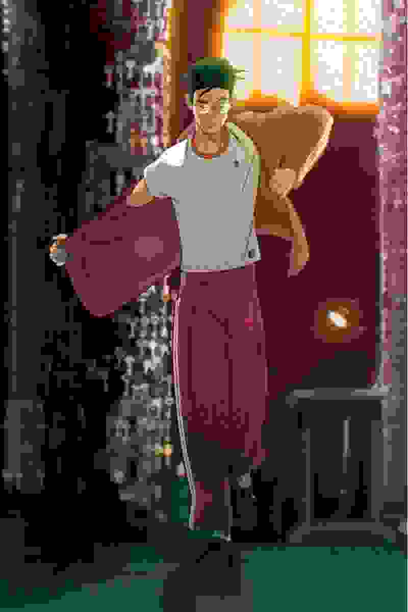 A young man in casual clothing is walking down a dimly lit city street, carrying a large red bag or suitcase.