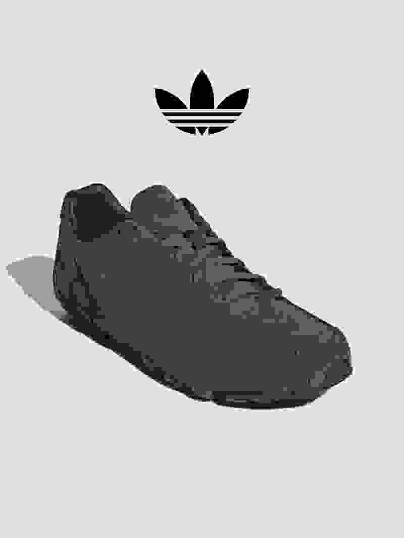 The image shows a pair of dark gray Adidas sneakers with the iconic Adidas trefoil logo prominently displayed in the background.