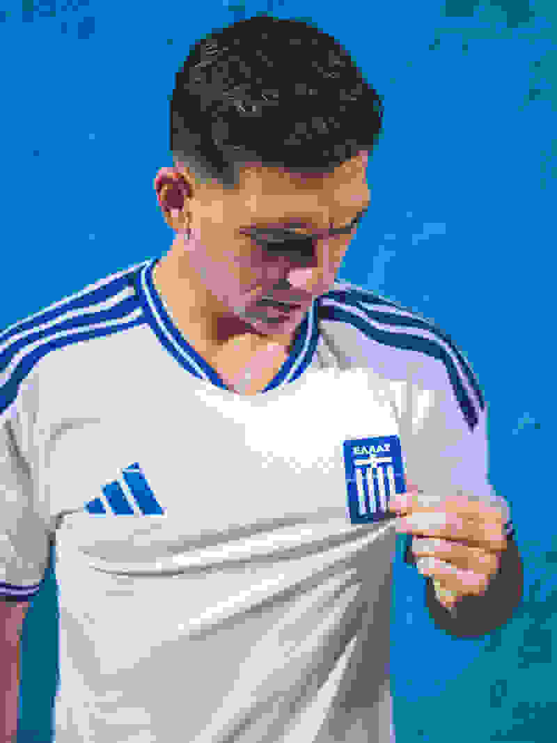 A young man wearing a white and blue soccer jersey stands in front of a vibrant blue background.