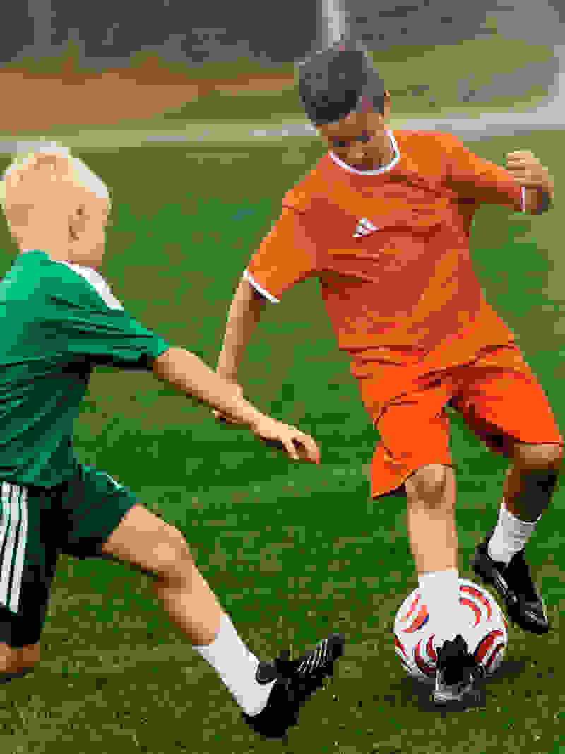 Two young boys in sports uniforms are playing soccer on a grassy field.