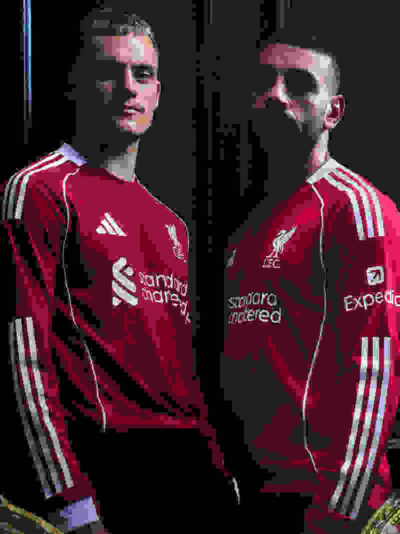 Two men wearing red Liverpool football jerseys stand in front of a dark background.