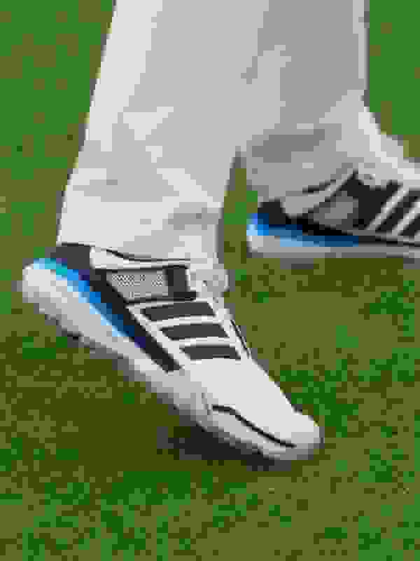 The image shows a person's feet wearing white and black athletic shoes standing on a grassy field.