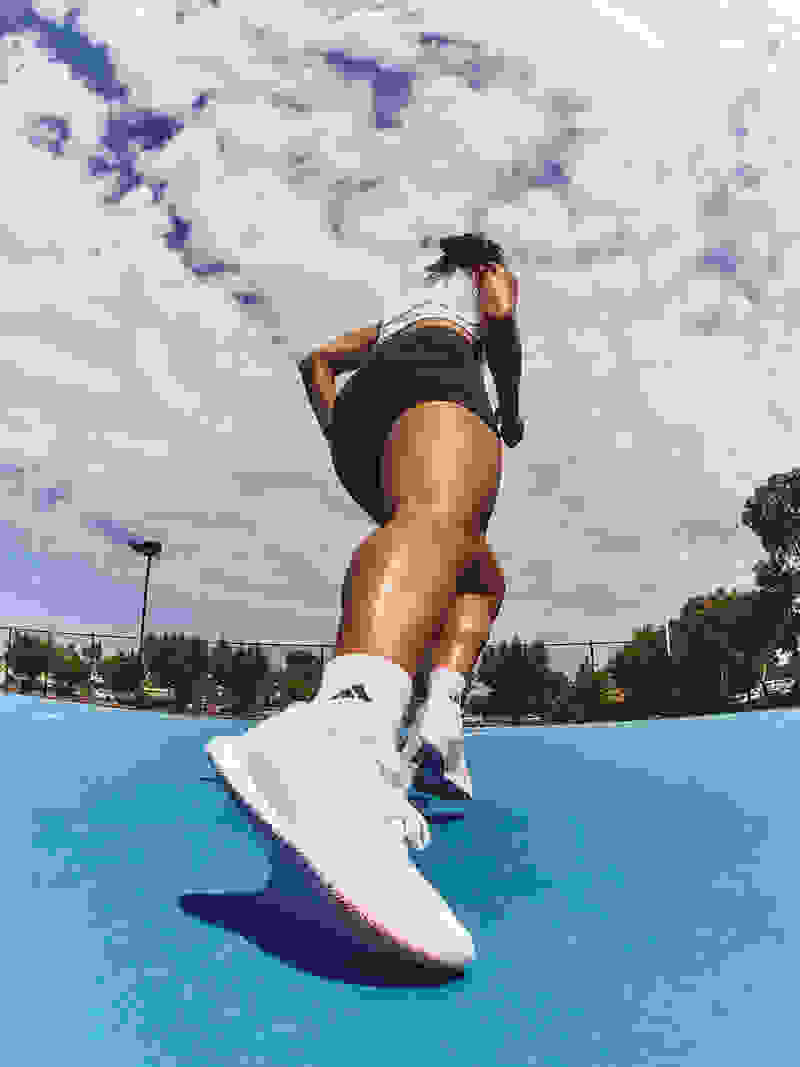 A person in athletic attire is jumping on a blue surface, with a cloudy sky visible in the background.