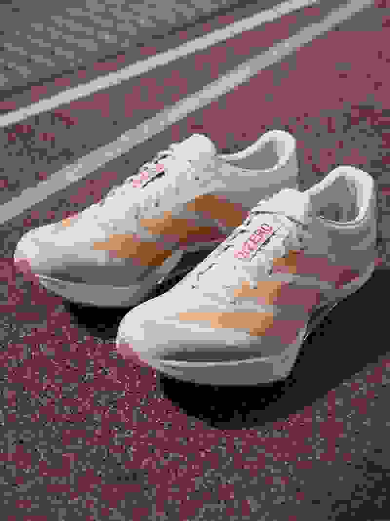 A pair of white and orange athletic shoes rests on a red and white running track.