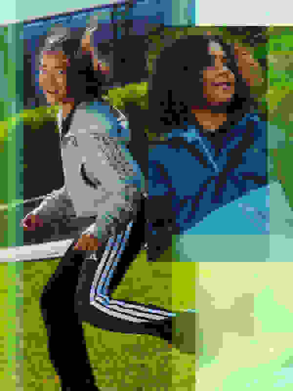 Twee jonge vrouwen met gekruld haar, de ene in een grijs jack en de andere in een blauw jack, staan voor een glazen gebouw dat wordt omgeven door groen.