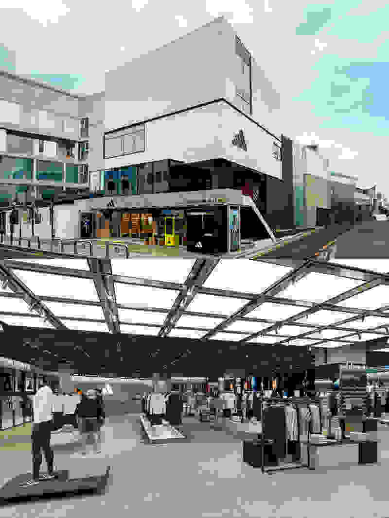 A modern, multi-story building with a glass and steel structure, surrounded by a covered walkway and various retail stores and shops in the foreground.