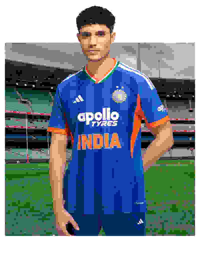 A young man wearing a blue and orange striped jersey stands on a sports field with a stadium visible in the background.