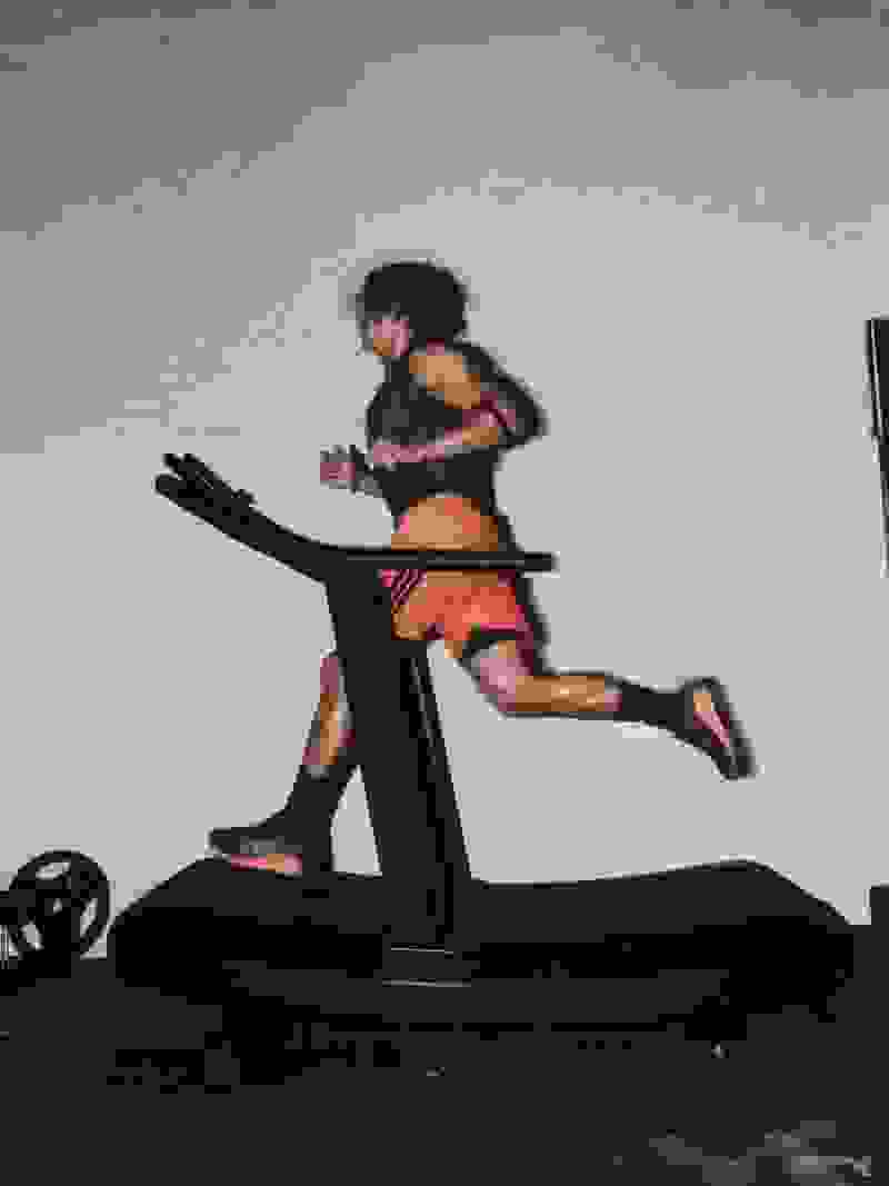 A person in athletic attire is running on a treadmill against a plain, light-colored wall.