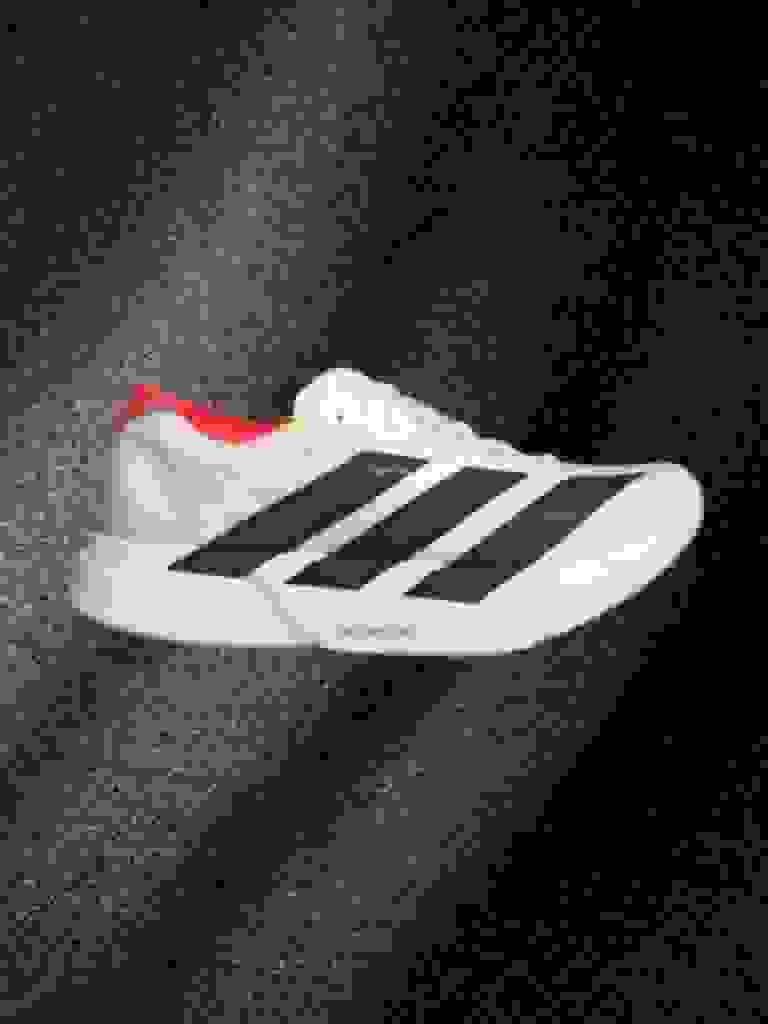 A white and black athletic shoe with red accents is displayed against a dark, textured background.