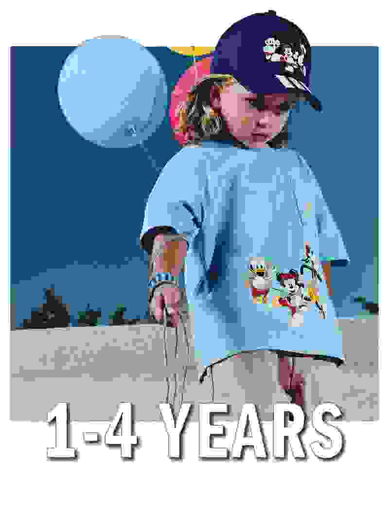 A young child wearing a blue shirt and a baseball cap holding a large blue balloon, with a colorful background of a clear sky and a concrete wall.