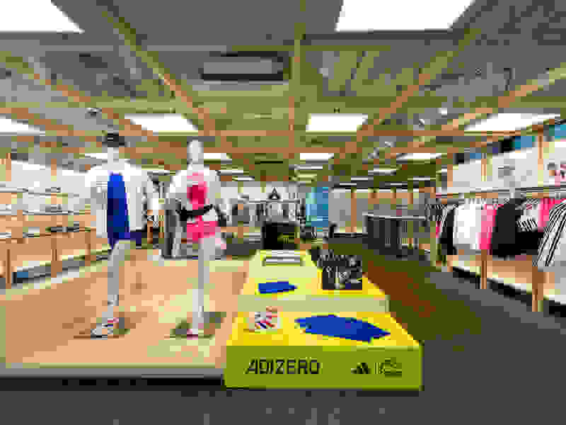 The image depicts a retail clothing store with various apparel and accessories displayed on shelves and mannequins. The foreground features a display platform with the Adidas logo, while the background shows the store's interior with a high ceiling, lighting fixtures, and a variety of clothing items available for purchase.