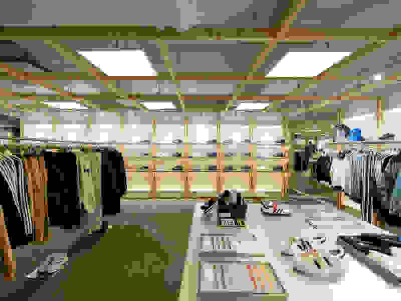 A spacious clothing store with wooden shelves and racks displaying a variety of apparel and accessories, including shoes, in a well-lit and organized retail environment.