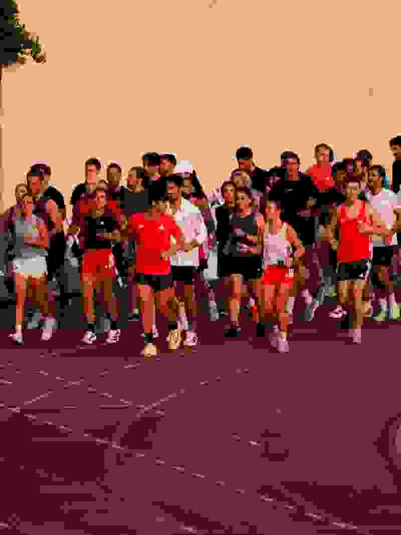 A group of people, mostly wearing red shirts, are running on a red track surrounded by a concrete wall in the background.