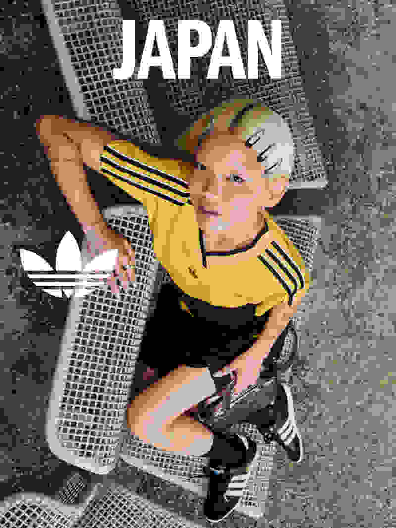 A young child wearing a yellow and black sports jersey sits on a gray mat with the word "JAPAN" prominently displayed in the background.