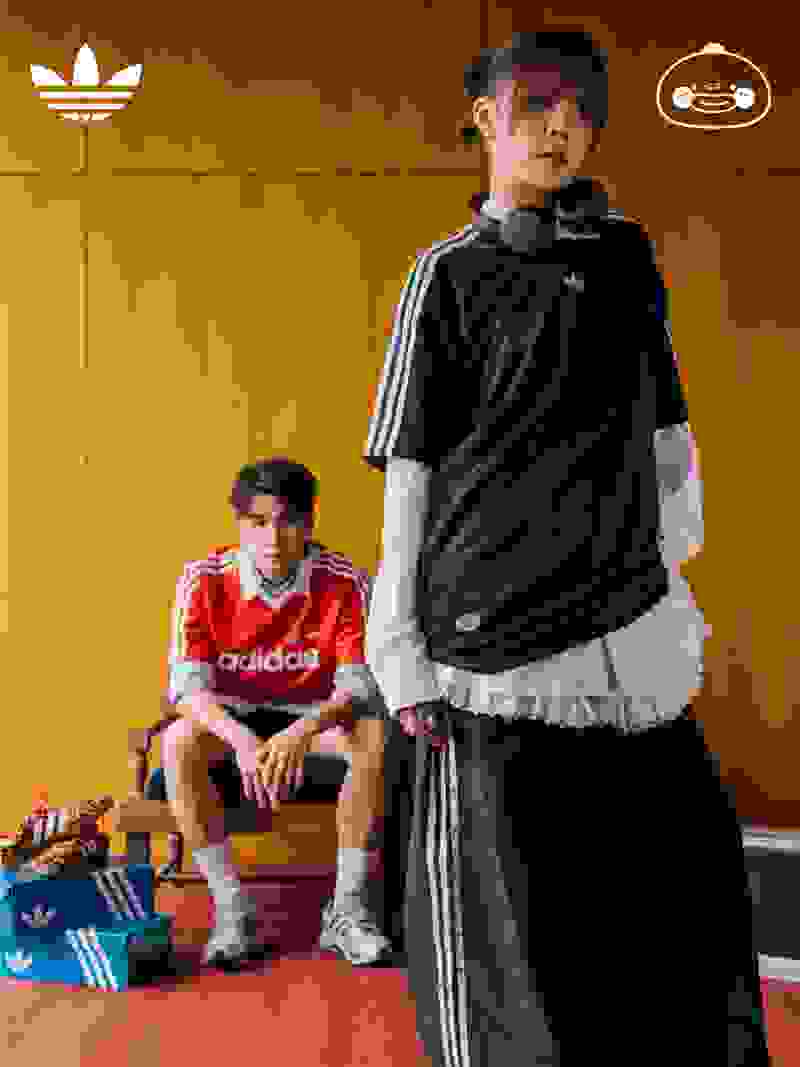 Two young individuals, one standing and one sitting, wearing Adidas sportswear against a wooden background with Adidas and gaming console logos.