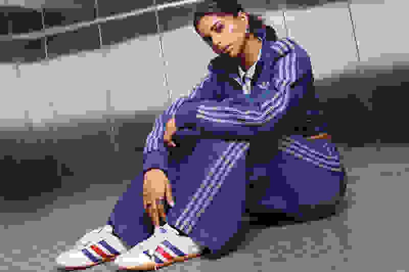 A woman in a blue and white striped tracksuit is sitting on the floor of what appears to be a tiled hallway or corridor.