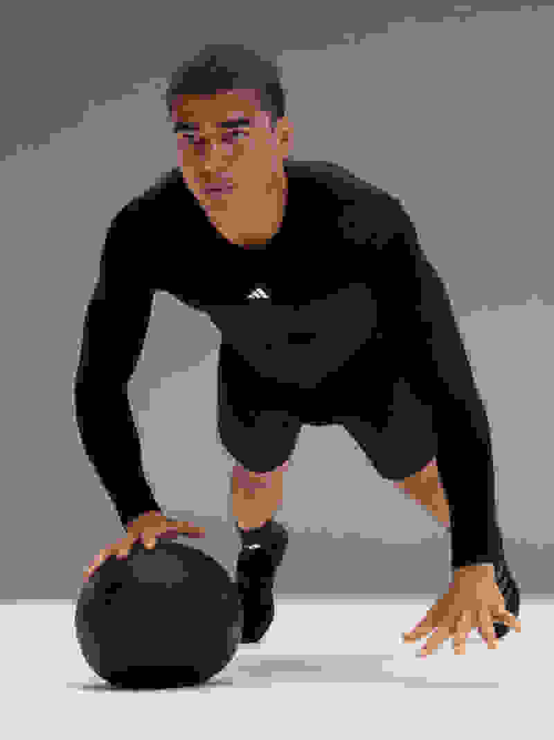 Man wearing adidas training gear performs press-ups with medicine ball.