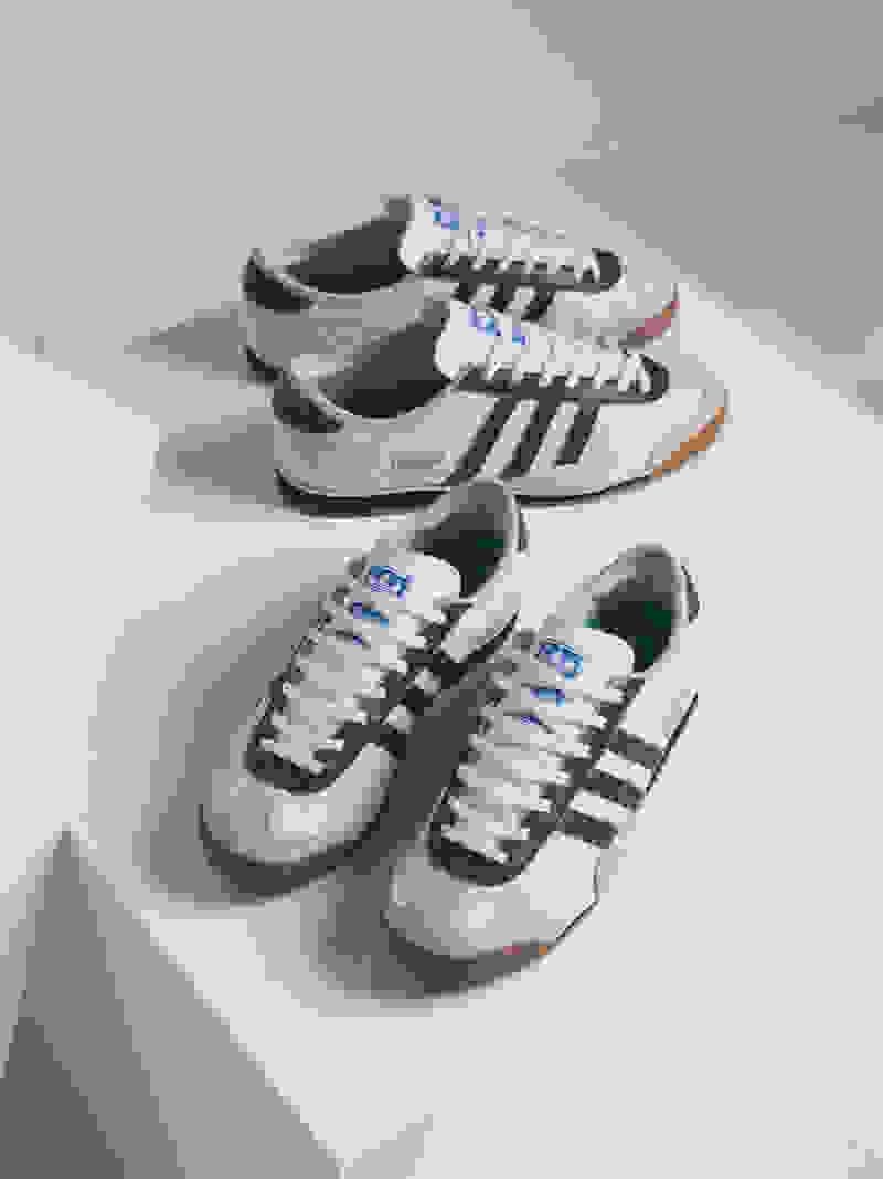 A pair of green and white Adidas sneakers are displayed on a white surface, with a simple and minimalist background.