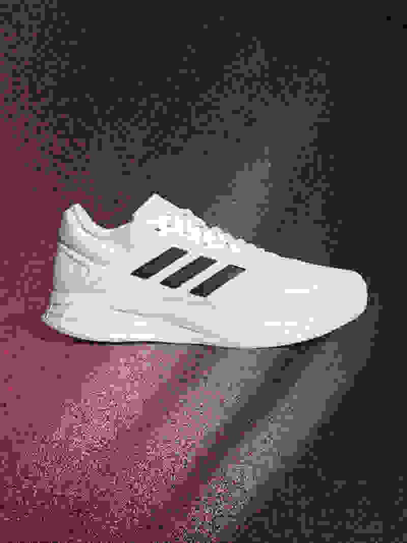 A white and black athletic shoe is prominently displayed against a dark, textured background with a reddish hue.