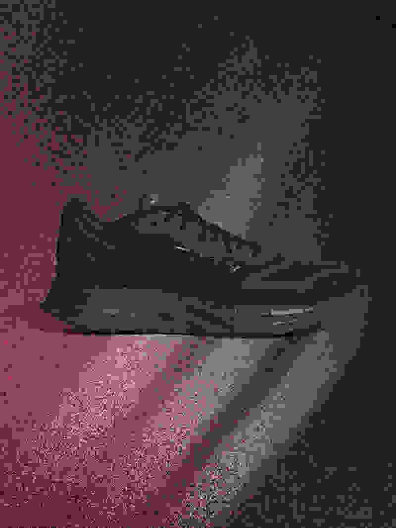 A sleek, all-black athletic shoe is prominently displayed against a dark, moody background with hints of red.
